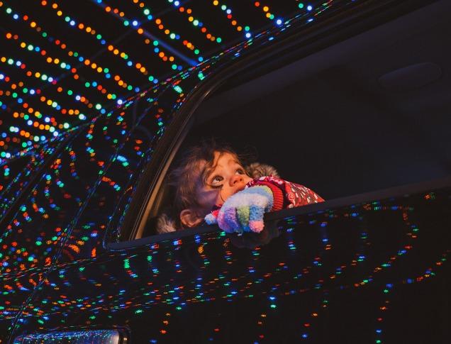 Young girl looking out of car window at glistening light displays