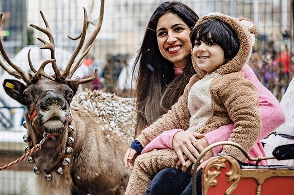 A mother and her child on a red sleigh with a deer in the background