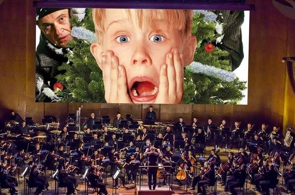 A large orchestra performing live on stage and behind them is a large screen showing a clip from the movie Home Alone