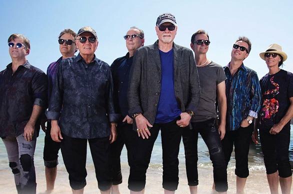 Members of the group The Beach Boys standing  on a beach with water in the distance