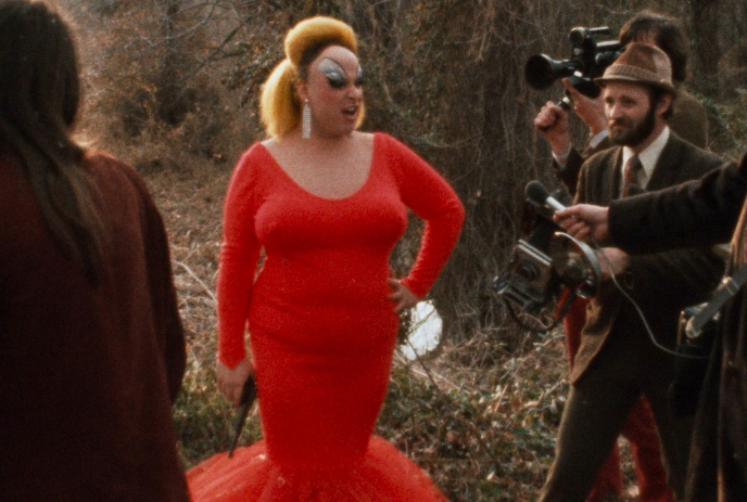 A person in a red dress is at a media event, surrounded by photographers and reporters.