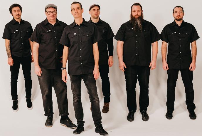 6 band members of The Planet Smashers all wearing black, posing for a photo against a white background.