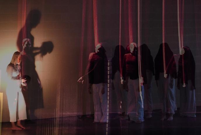 Figures fading into invisibility, dimly lit background with vertical lines and shadows from a theater set.