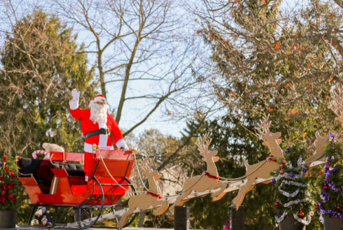 Santa Claus in a red sleigh pulled by reindeer, set outdoors with trees and clear skies, capturing festive holiday spirit.