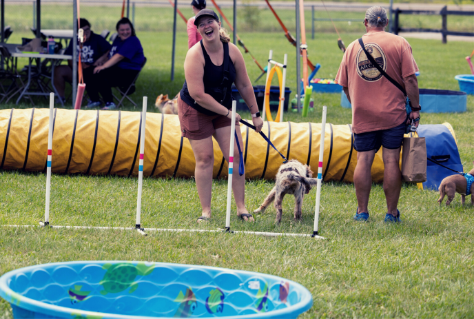 Girl laughing as she and her dog are on an outdoor dog obstacle course.