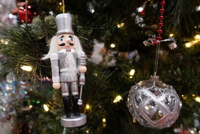 A silver nutcracker ornament and a decorative silver bauble hang on a lit Christmas tree.