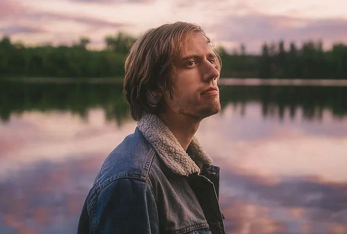 Aleksi Campagne in front of a pond at sunset, with trees in the background.