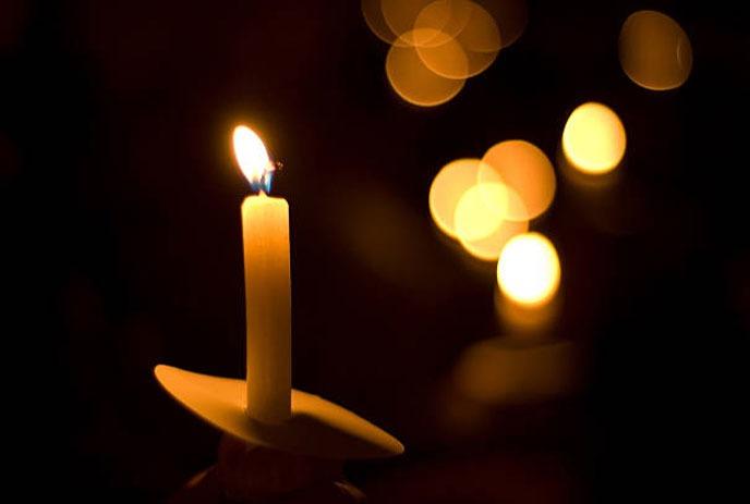 A lit candle in a dark room, with candle light in the background.