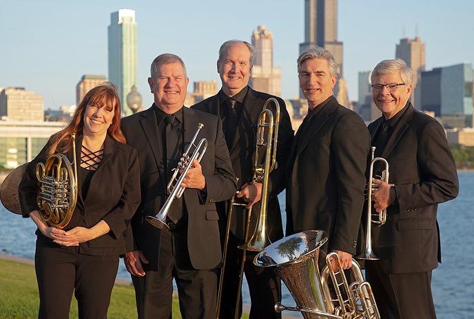 Brass quintet smiling for the picture with their instruments under a city skyline in the background