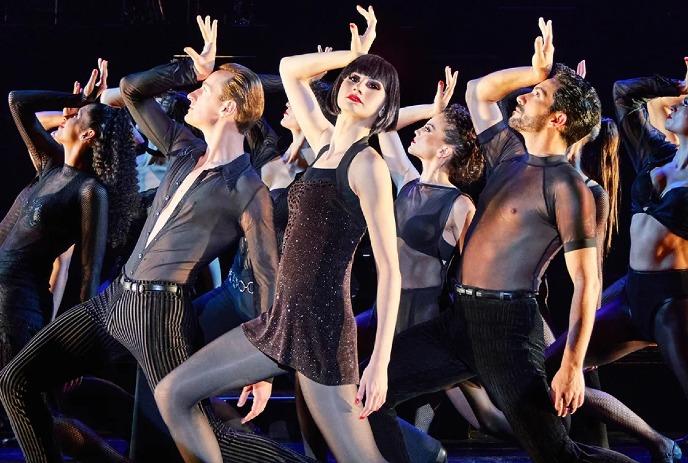 Performers in black attire strike dramatic poses on stage during a production of the musical 'Chicago'.