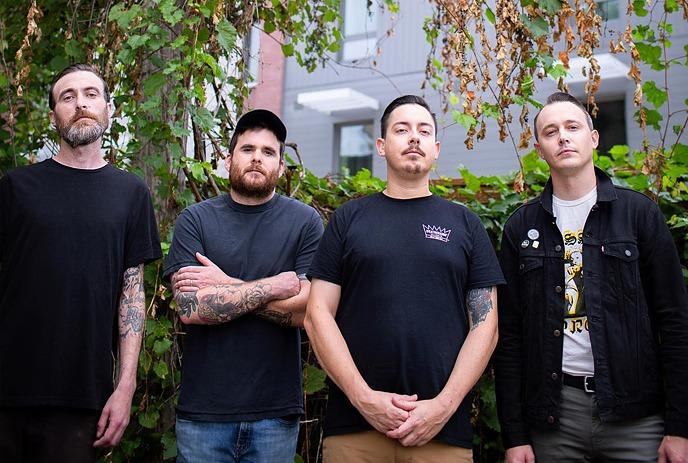 An outdoor photo of The Flatliners standing in front of greenery.