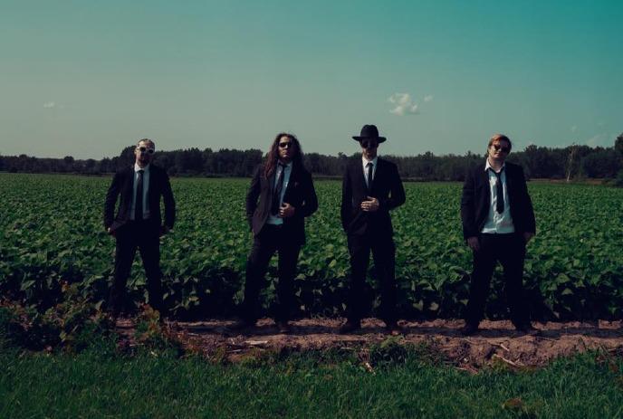 The 4 band members of Hartlet, standing in a farm field wearing suites.
