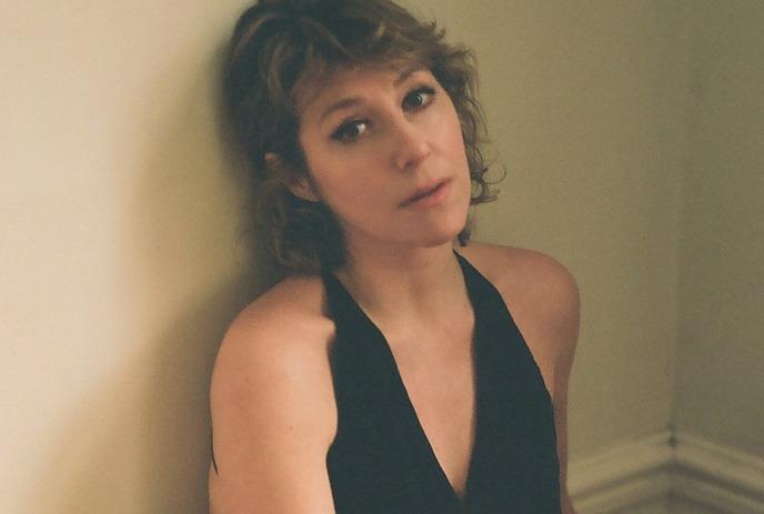 Musician Martha Wainwright in a black outfit sits against an off-white wall.