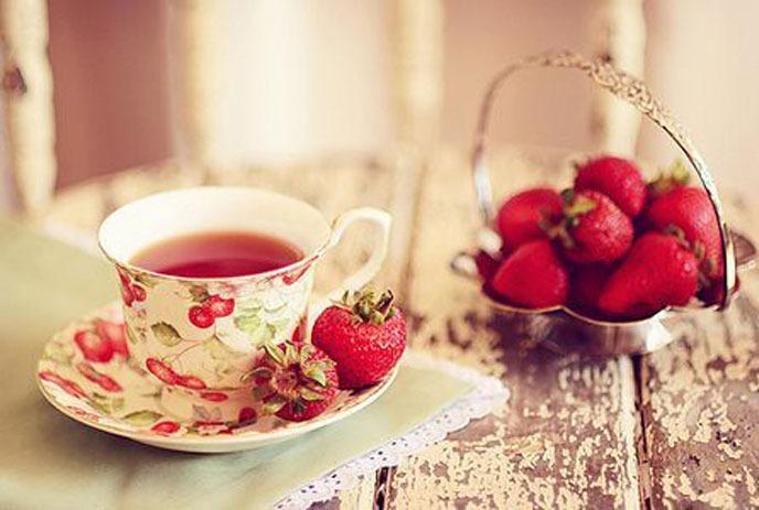 A teacup with tea in it, next to strawberries on a table.