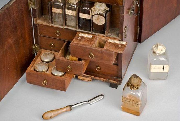 A vintage wooden apothecary kit with glass bottles, metal tins, drawers, and a small spatula tool.