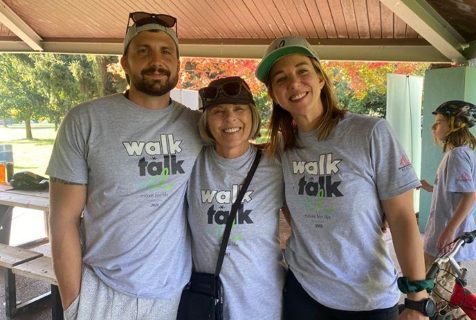 A man and two ladies smiling in “walk & talk” t-shirts at an outdoor event, promoting health and wellness.