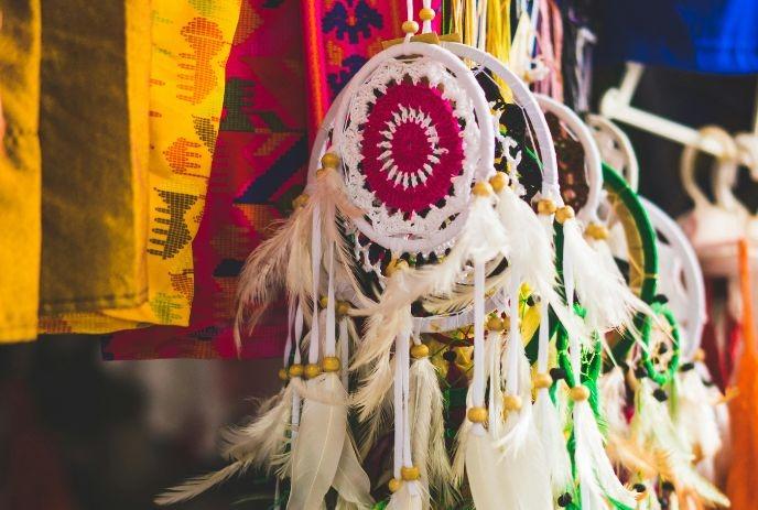 Colorful dreamcatchers with feathers hanging in a row, alongside vibrant textiles.