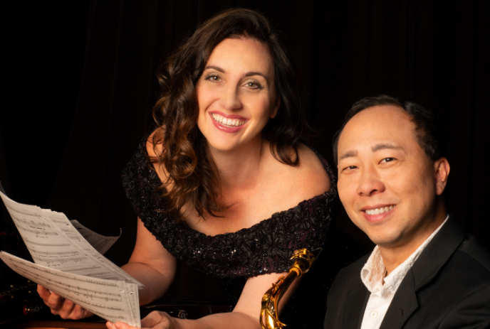 Kenneth and Casey Tse, smiling while holding sheet music against a black background.