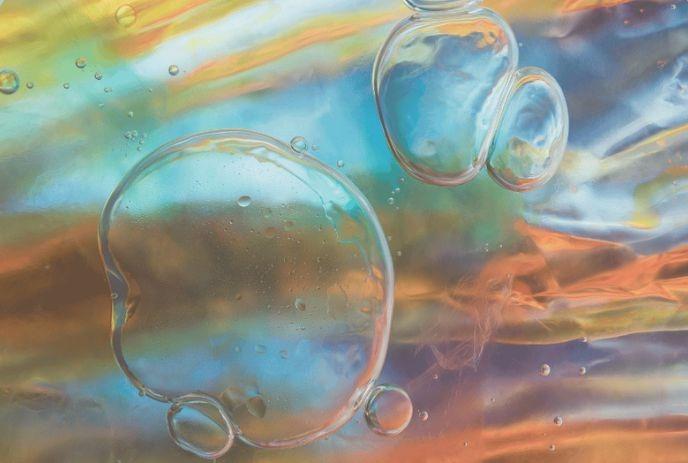 A close-up image of colorful soap bubbles on an iridescent background, showing a mix of blue, orange, and green hues.