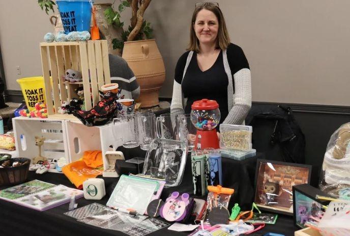 Table with clear glassware, colorful trinkets, and assorted merchandise on display by a women.