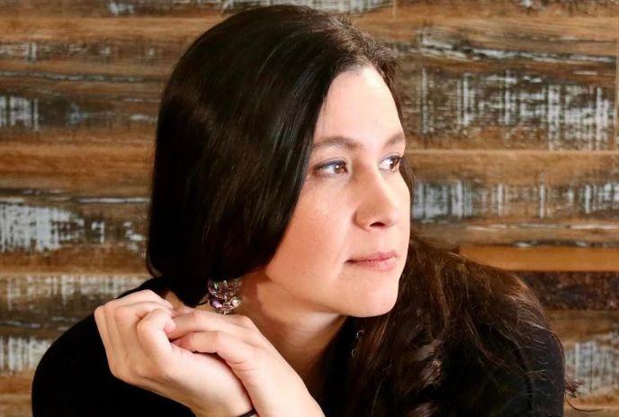 A portrait picture of Katherena Vermette wearing a black dress and looking at her left with a woody background.