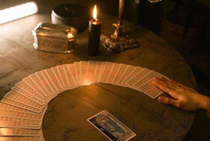 Tarot card reading setup with cards, a lit candle, and a hand on a round table creating a mystical atmosphere.