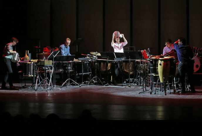 A group of five musicians playing various percussion instruments including congas, bongos, marimbas, and xylophones.