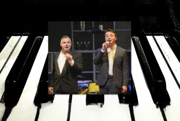 Two men in suits are singing on stage, positioned in the center of a background featuring black and white piano keys.
