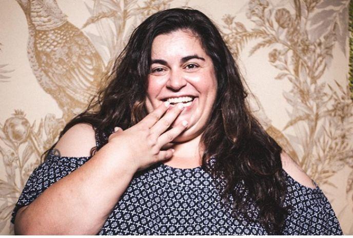 Debra DiGiovanni putting her hand over her face while laughing, in front of a floral pattern wall.