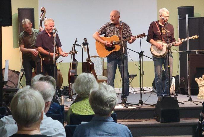 A band of four musicians is performing on stage with various string instruments, including guitars and a banjo.