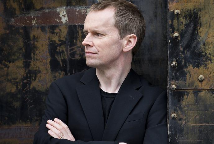 Steven Osborne standing in front of a rusty metal wall, looking sideways.