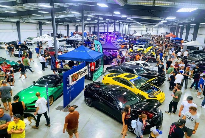 An indoor car show with a variety of vehicle in different colors like green, yellow, black and attendees.