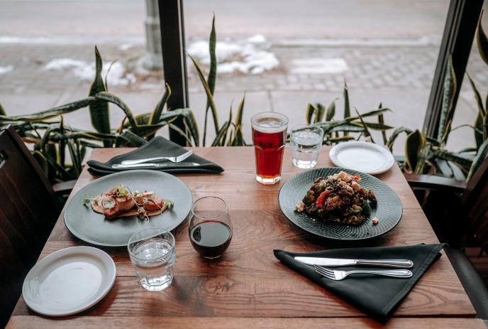 A table at Abruzzi restaurant set with gourmet dishes and drinks against a backdrop of a window and plants.