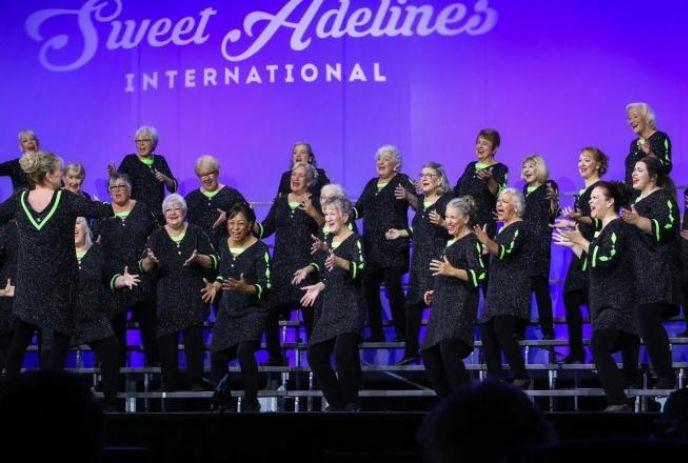 A group of people performing on stage in matching black outfits, with lively expressions and movements.