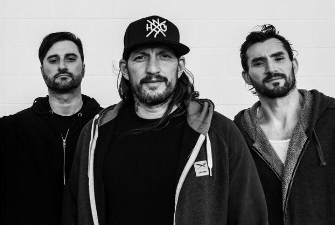 Three male members of the band Madball stand side by side against a white brick wall in a black-and-white photo.