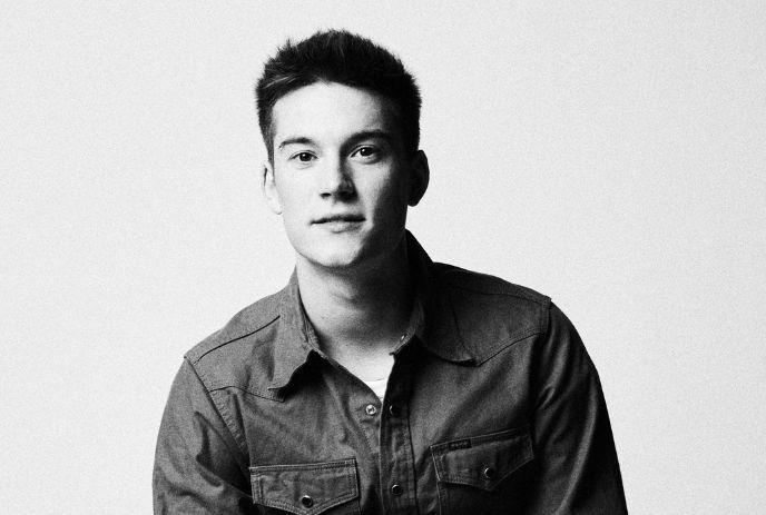 Cameron Whitcomb in a button-up shirt with chest pockets, sitting against a plain background. The image is black and white.