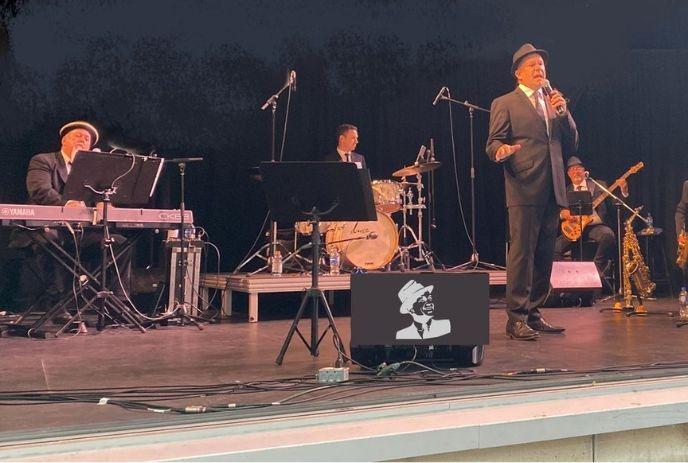 A band performing on the stage with their equipment while wearing the black suites and hats.