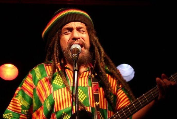 Errol 'Skippah' Blackwood performing on stage holding a guitar, wearing Jamaican clothes.