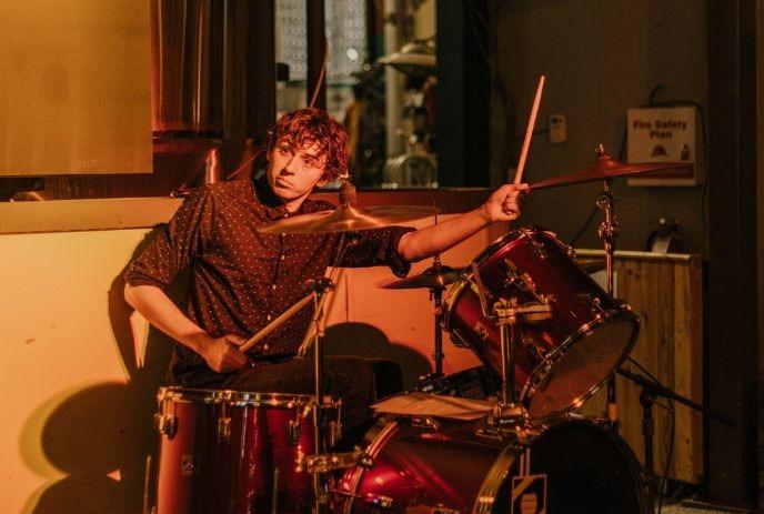 Drummer playing his drum sets passionately under soft yellow lightning.