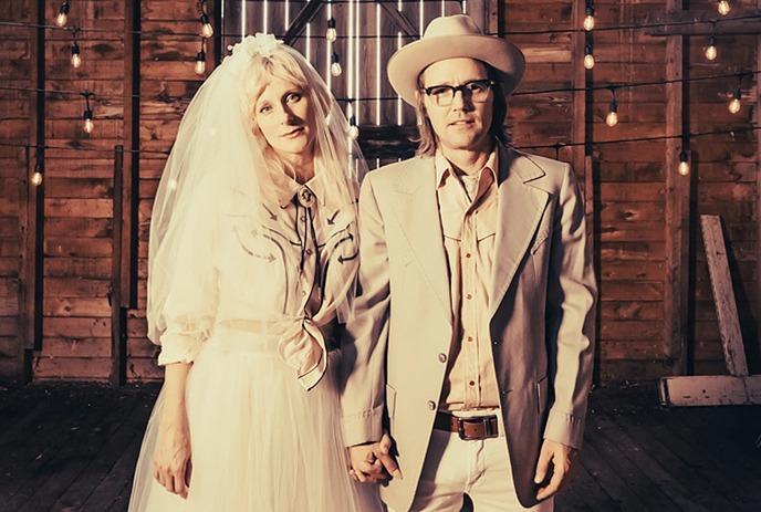 Melissa McClelland and Luke Doucet standing together in a barn wearing wedding clothes.