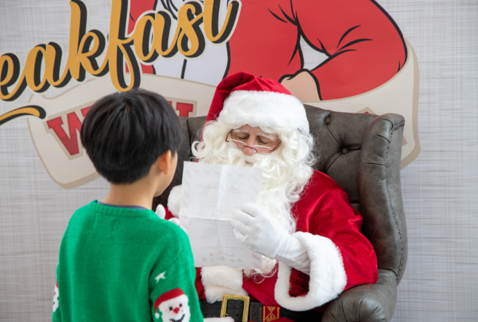 Santa Claus sitting down and reading a child's Christmas wish list in front of him.