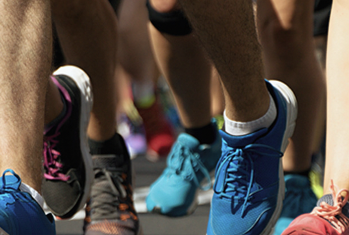 A close-up of several runners' feet in motion, wearing colorful running shoes, captured during a race on a paved road.