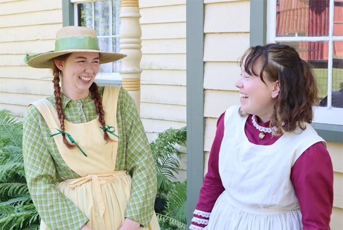 Two people are standing next to each other laughing, dressed as characters from Anne of Green Gables.