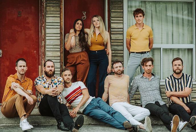 The 10 band members of Dwayne Gretzky, all posing in front of windows on a sunny day.