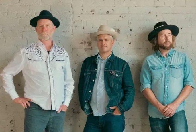 The 3 band members of Elliott Brood, wearing hats and posing against a white wall.