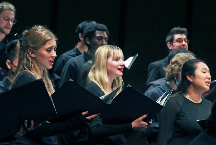 A choir performs passionately on stage, with members holding music sheets as they sing.