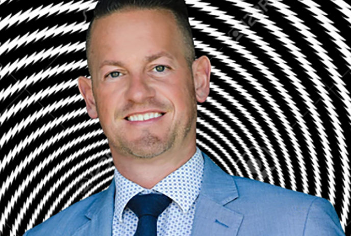 Person wearing a suit and smiling with a black and white optical illusion in the background.