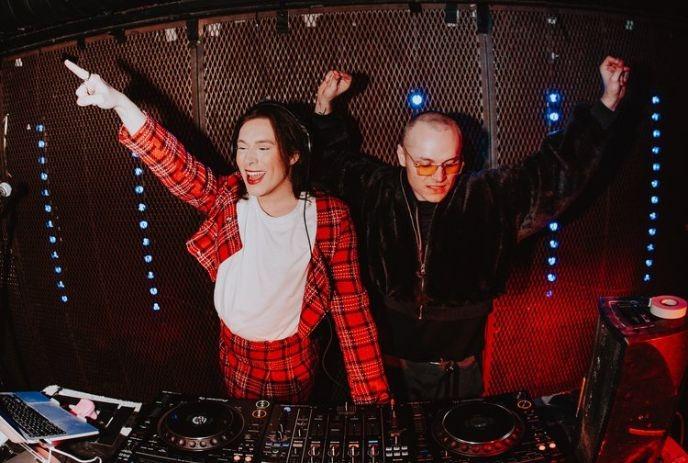 Two DJ's playing their music system while enjoying the atmosphere under a dark background and blue light stripes.