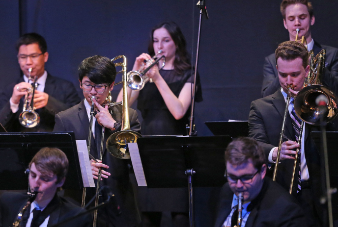 Musicians with brass instruments on stage, performing in an ensemble. The scene captures artistic collaboration.