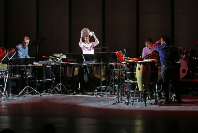 A band on stage with various percussion instruments, including drums and cymbals, during a performance.